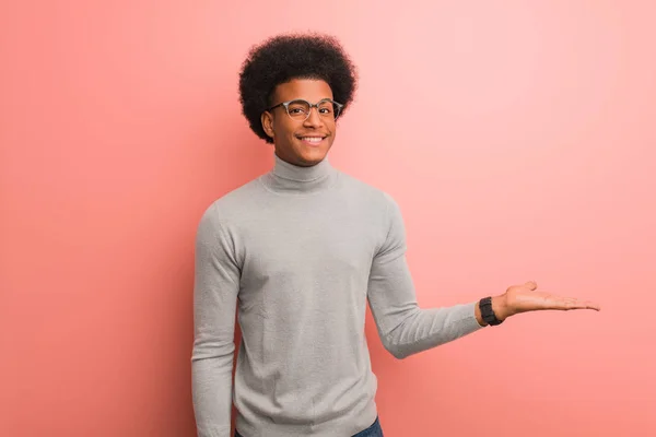 Jovem Afro Americano Sobre Uma Parede Rosa Segurando Algo Com — Fotografia de Stock