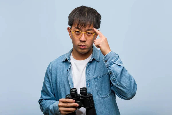 Young chinese man holding a binoculars thinking about an idea