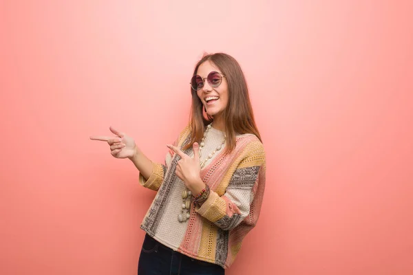 Young hippie woman on pink background pointing to the side with finger