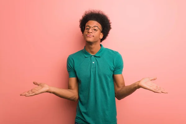 Joven Afroamericano Sobre Una Pared Rosa Dudando Encogiéndose Hombros — Foto de Stock