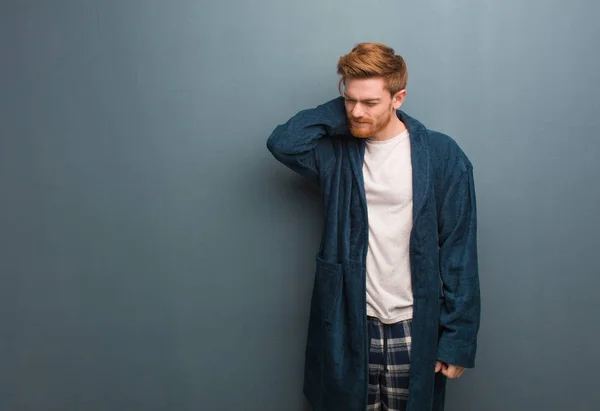 Young redhead man in pajama suffering neck pain