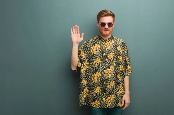 Young redhead man wearing exotic summer clothes showing number five