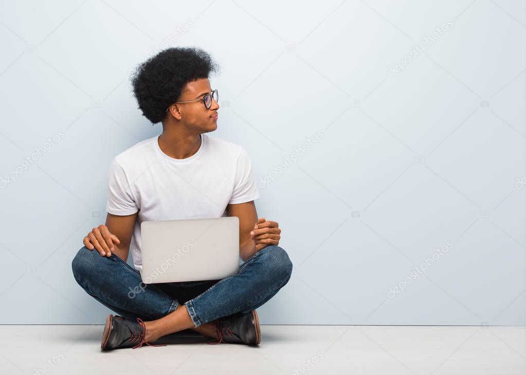 Young black man sitting on the floor with a laptop on the side looking to front