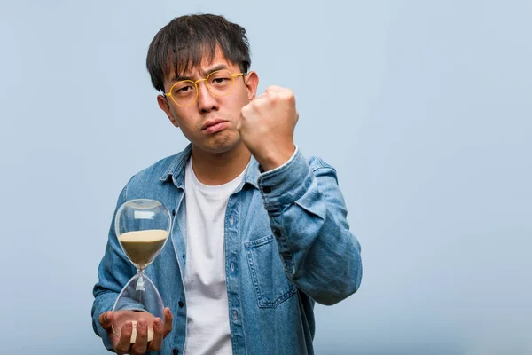 Joven Chino Sosteniendo Temporizador Arena Mostrando Puño Frente Expresión Enojada —  Fotos de Stock