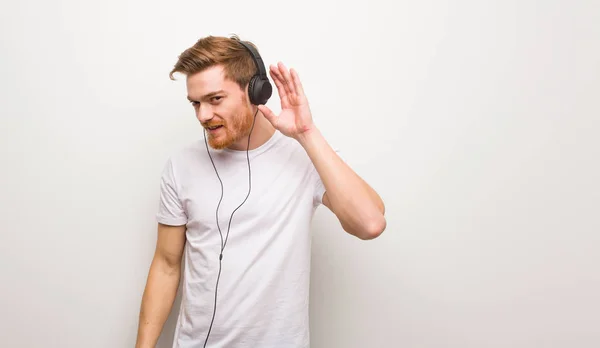 Young redhead man try to listening a gossip. Listening to music with headphones.
