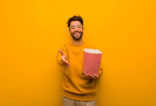 Young man holding popcorns reaching out to greet someone