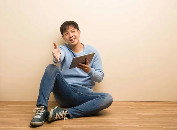 Young chinese man sitting using his tablet reaching out to greet someone