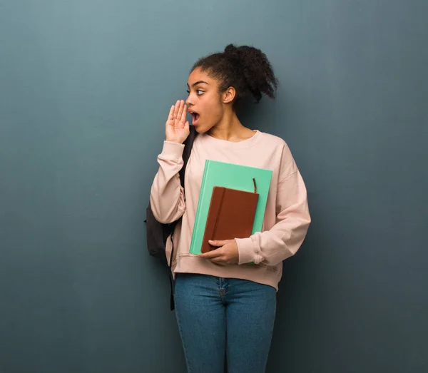 Young student black woman whispering gossip undertone. She is holding books.