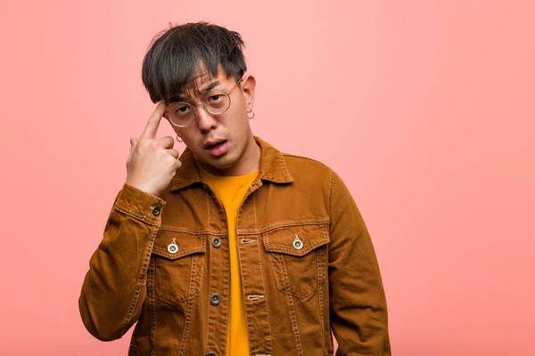 Young chinese man wearing a jacket doing a disappointment gesture with finger