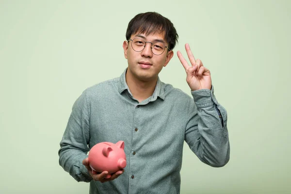 Ung Asiatisk Mand Holder Sparegris Bank Viser Nummer - Stock-foto