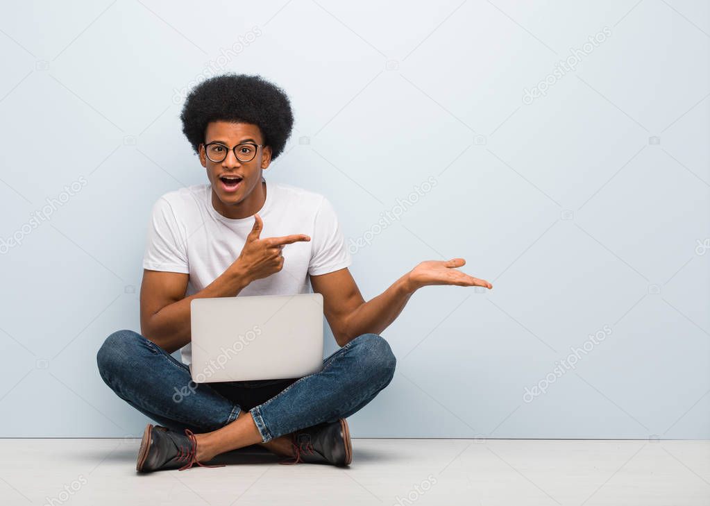 Young black man sitting on the floor with a laptop holding something with hand