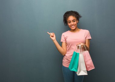 Genç siyah kadın parmakla yan gösteren. Elinde bir alışveriş çantası var..