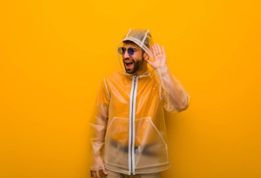 Yağmurluk giyen genç adam bir dedikoduyu dinlemeye çalış.