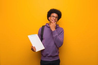 Genç Afro-Amerikan öğrenci elinde bir not panosuyla rahatlamış fotokopi odasına bakan bir şey düşünüyor.