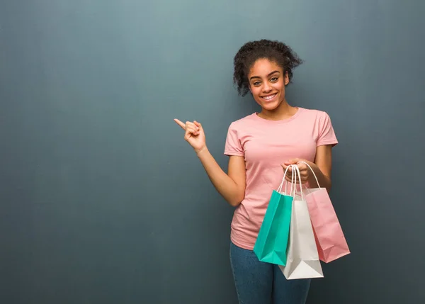 Young black woman pointing to the side with finger. She is holding a shopping bags.