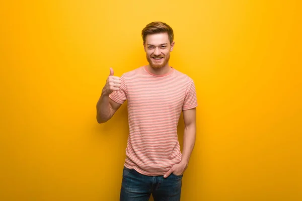 Young redhead man smiling and raising thumb up