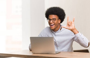 Genç siyah adam dizüstü bilgisayarını kullanarak taş hareketi yapıyor.