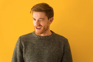 Genç kızıl saçlı adam göz kırpıyor, komik, arkadaşça ve kaygısız bir jest yapıyor.