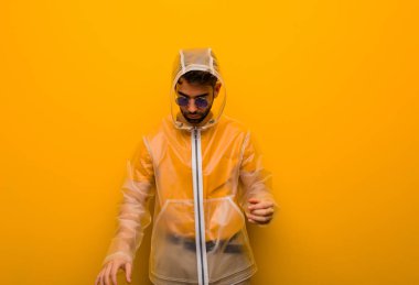 Yağmurluk giyen genç adam yorgun ve çok uykulu.