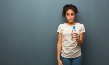 Genç siyahi kadın bir fikir düşünüyor. Elinde bir su şişesi var..