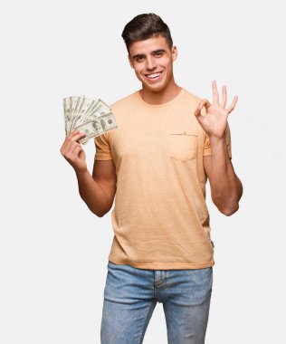 Neşeli ve kendine güvenen ok jest yapıyor dolar tutan genç adam