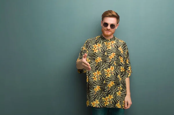 Young redhead man wearing exotic summer clothes reaching out to greet someone
