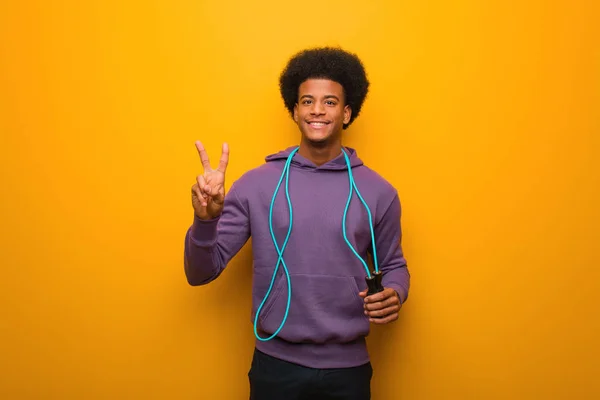 Young african american sport man holding a jump rope showing number two