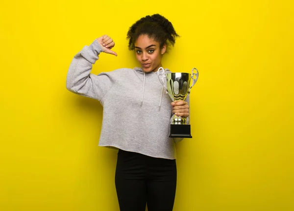 Young fitness black woman pointing fingers, example to follow. Holding a trophy.