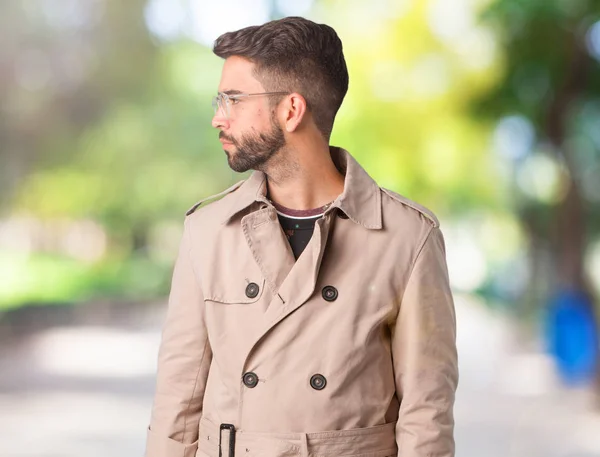Young man wearing trench coat on the side looking to front