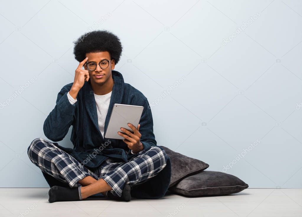 Young black man sitting on his house and holding his tablet thinking about an idea