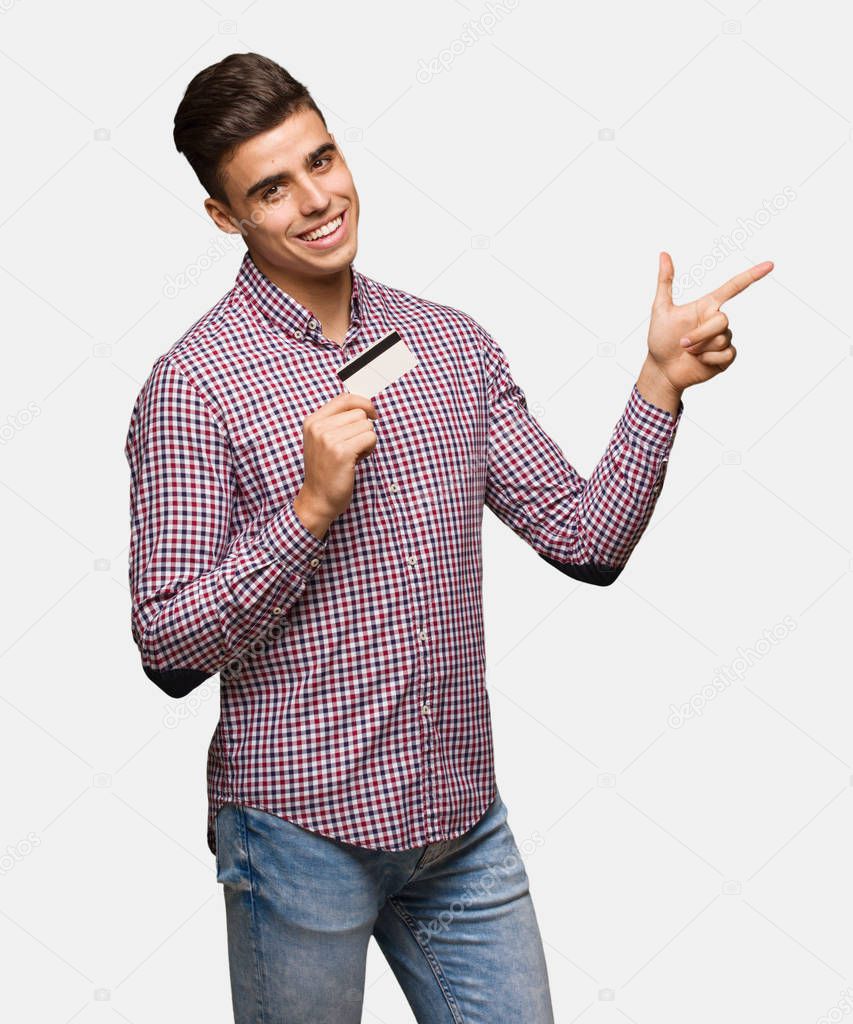 Young man holding credit card pointing to the side with finger