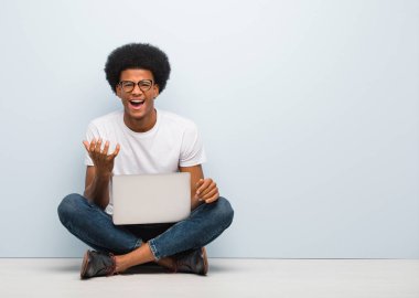 Genç siyah bir adam dizüstü bilgisayarla yerde oturuyor çok korkmuş ve korkmuş.