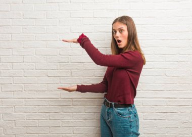 Tuğla duvarın üzerinde elinde çok şaşırmış ve şok olmuş bir şey tutan genç bir kadın.