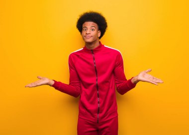 Turuncu bir duvarın üzerinden omuzlarını silkeleyen genç bir zenci.