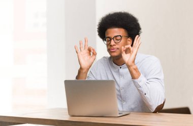 Genç siyah adam yoga yaparken dizüstü bilgisayarını kullanıyor.