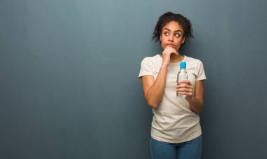 Genç siyahi kadın bir fikir düşünüyor. Elinde bir su şişesi var..