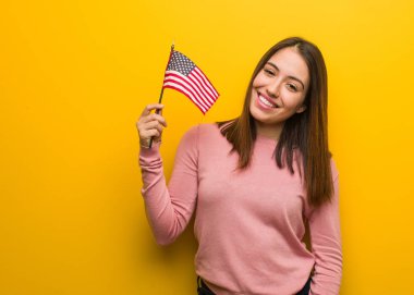 Amerika Birleşik Devletleri bayrağını elinde tutan genç, sevimli bir kadın. Kocaman bir gülümsemesi olan.