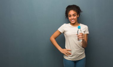 Kalçasında elleri olan genç siyahi bir kadın. Elinde bir su şişesi var..