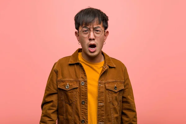 Young chinese man wearing a jacket screaming very angry and aggressive