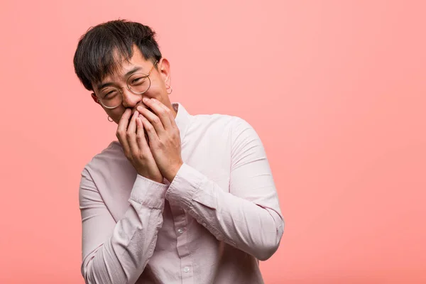 Young chinese man laughing about something, covering mouth with hands