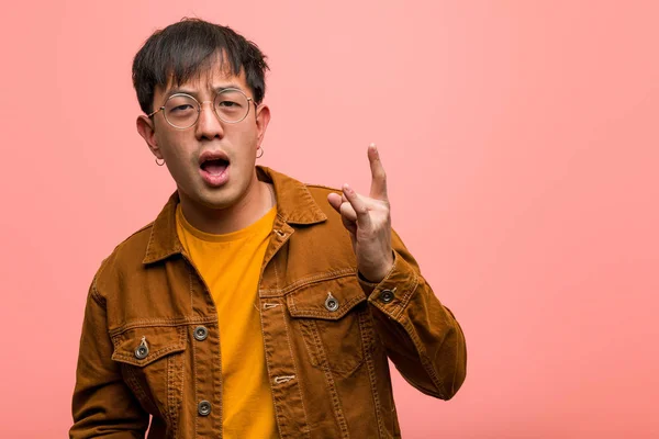 Young chinese man wearing a jacket doing a rock gesture