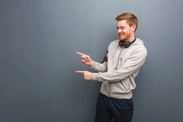 Young fitness redhead man pointing to the side with finger
