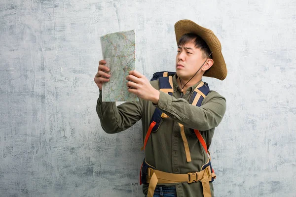 Young chinese explorer man holding a map doubting and confused