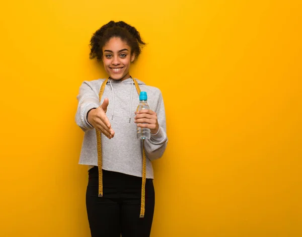 Young fitness black woman reaching out to greet someone.Holding a water bottle.