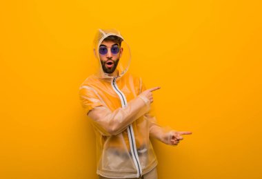 Genç adam parmak ile yan işaret eden bir yağmur ceket giyiyor