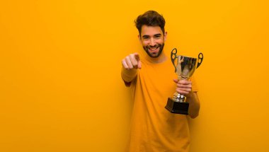 Elinde bir kupa tutan genç adam neşeli ve gülümsüyor.