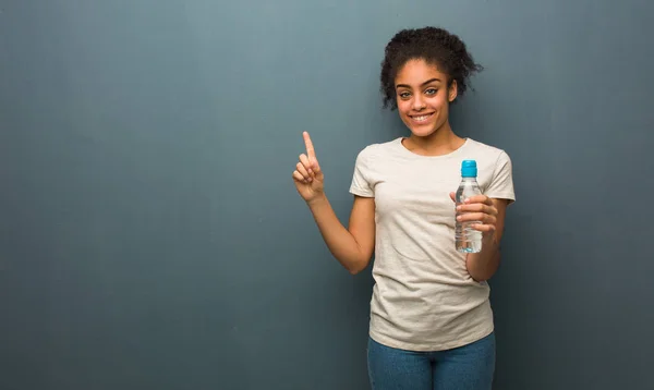 Молодая Черная Женщина Показывает Номер Один Держит Бутылку Водой — стоковое фото