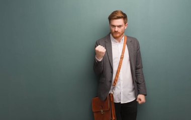 Genç kızıl saçlı iş adamı yumruğunu öne doğru gösteriyor, kızgın bir ifade.