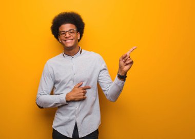 Turuncu bir duvarın üzerinde parmakla yan gösteren genç afro-amerikan adam