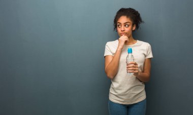 Genç siyahi kadın şüpheci ve kafası karışık. Elinde bir su şişesi var..